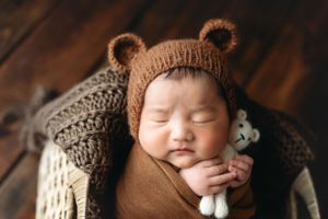 An Asian baby wearing a bear hat and holding a small cream bear. - Greenville SC newborn photographer - Easley SC newborn photographer