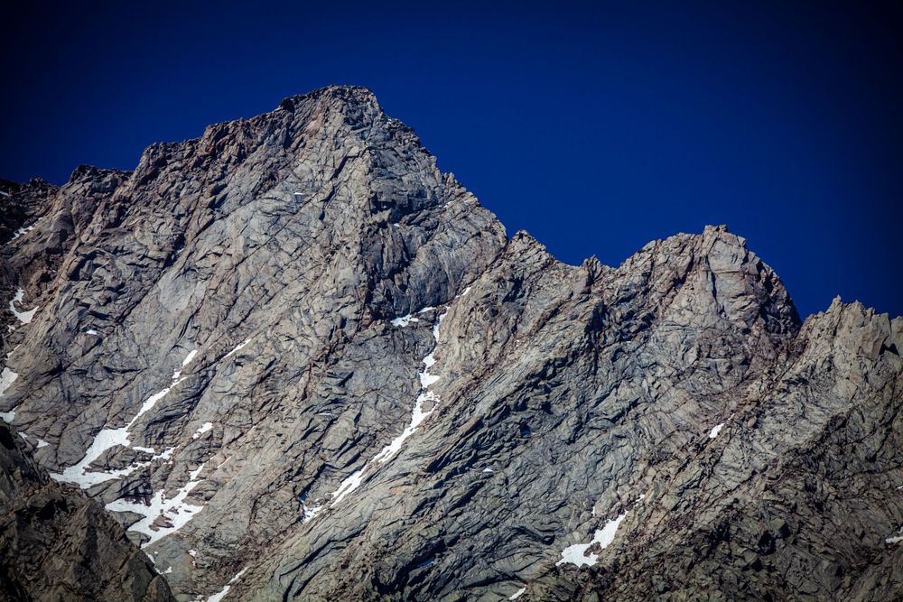 Close-up view of snow-dusted rocky mountain peaks against vibrant blue sky.