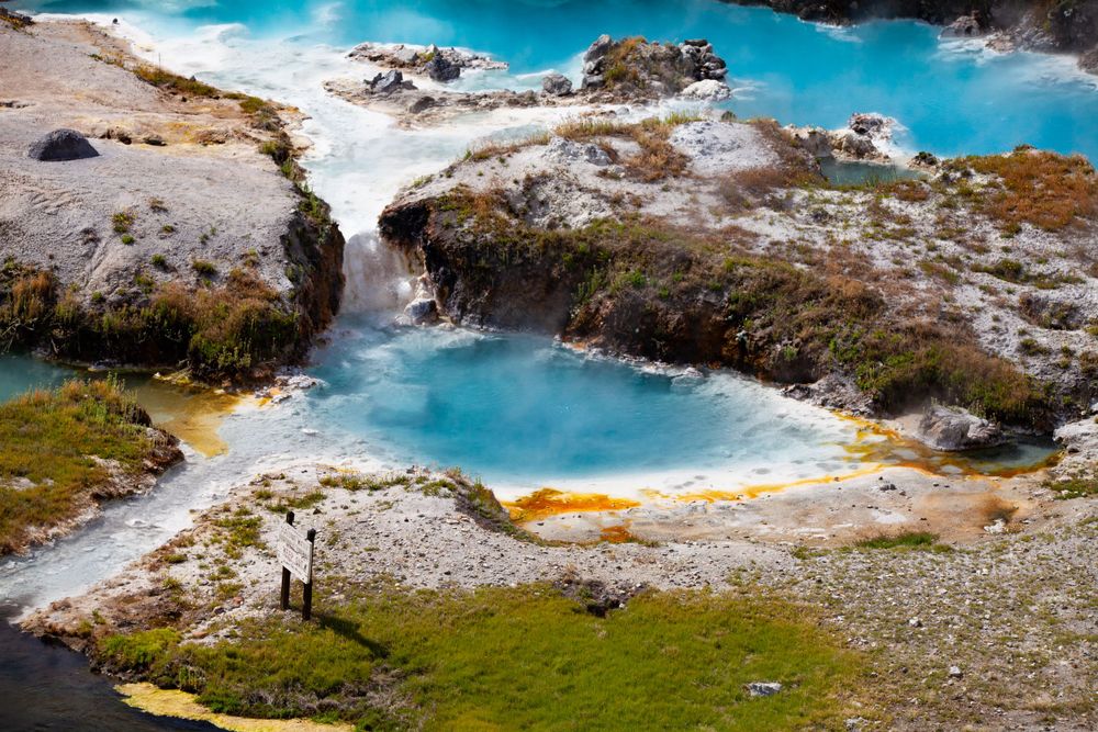 Turquoise geothermal pool with cascading waterfall among rocky terrain.
