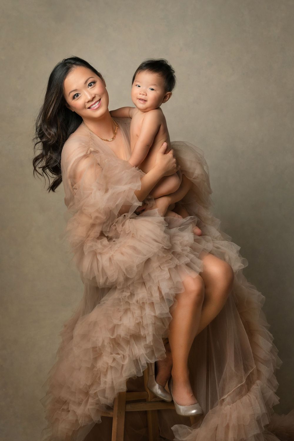 Elegant studio portrait of a mother in a flowing peach tulle gown and her adorable baby against neutral studio backdrop.