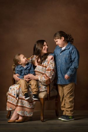 A warm studio portrait of a mother and her two sons sharing a candid moment on a vintage chair.