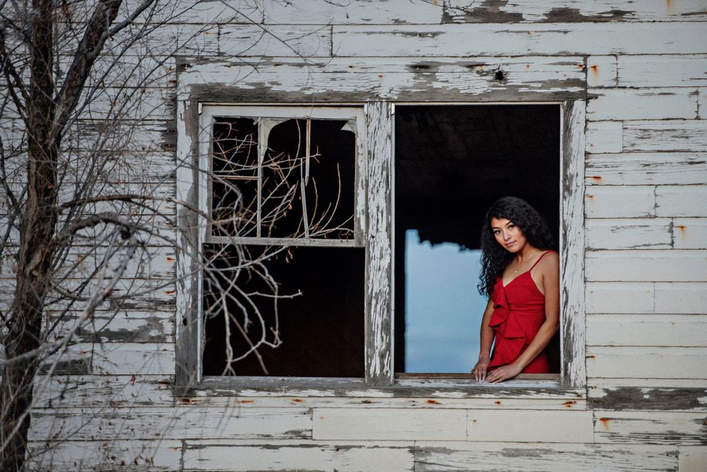 Young lady gazes out the window of an old house