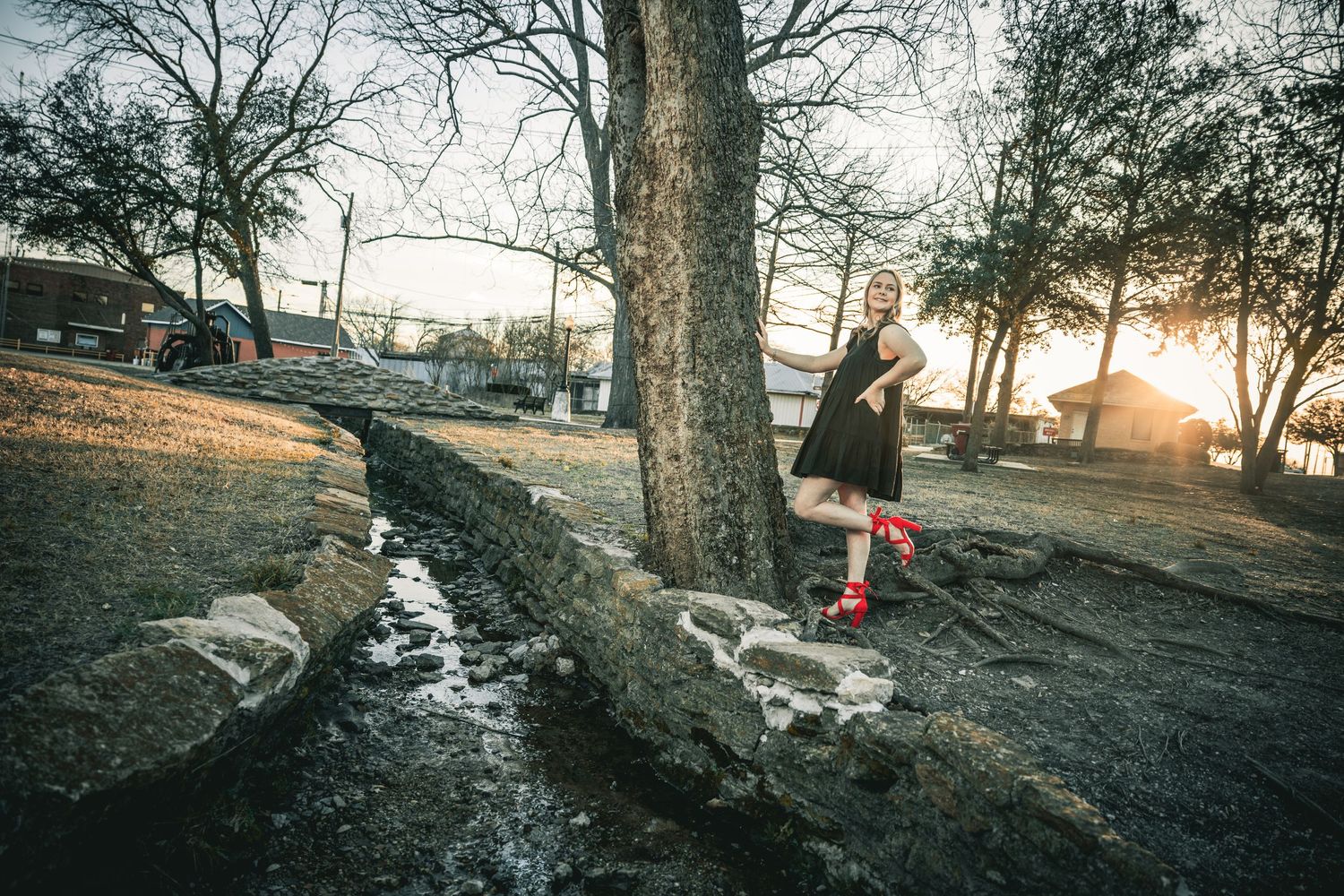 Person balancing on a wooden beam in a park during sunset while crossing a small stream.