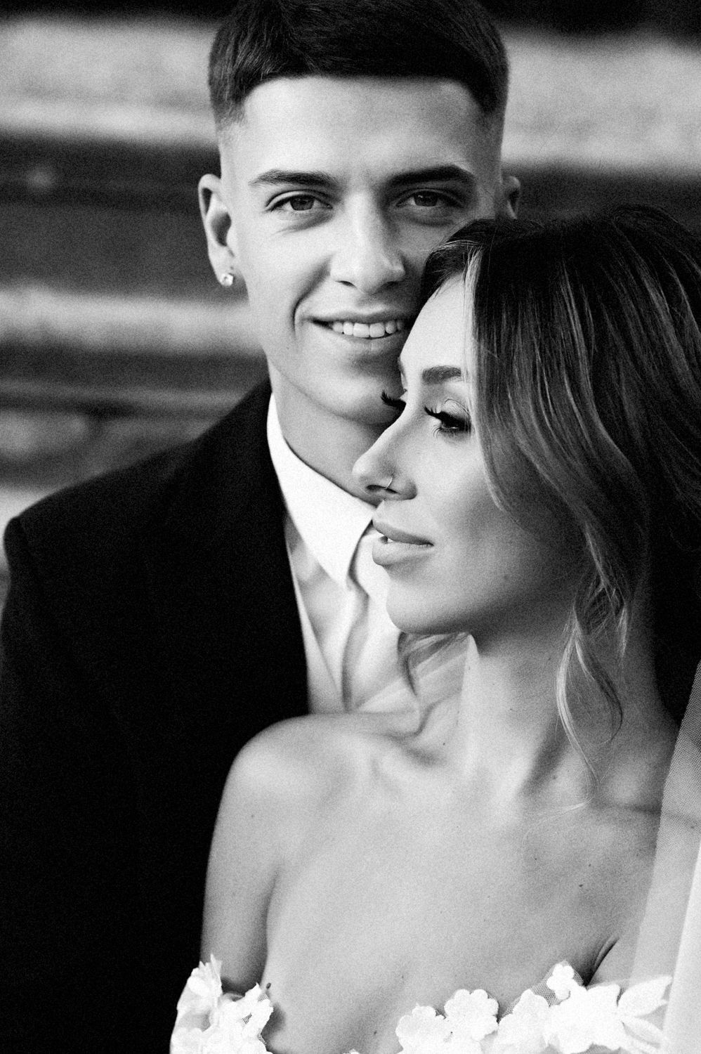 A close-up black and white portrait of a couple in elegant wedding attire.