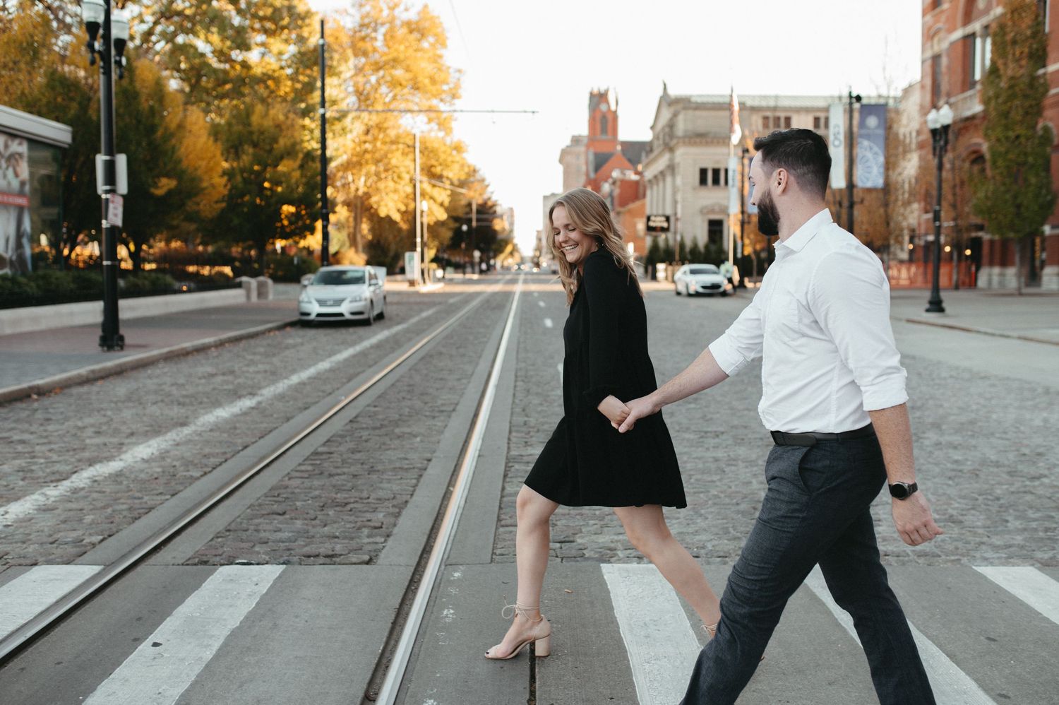 Stylish couple crossing urban street with trolley tracks during autumn.