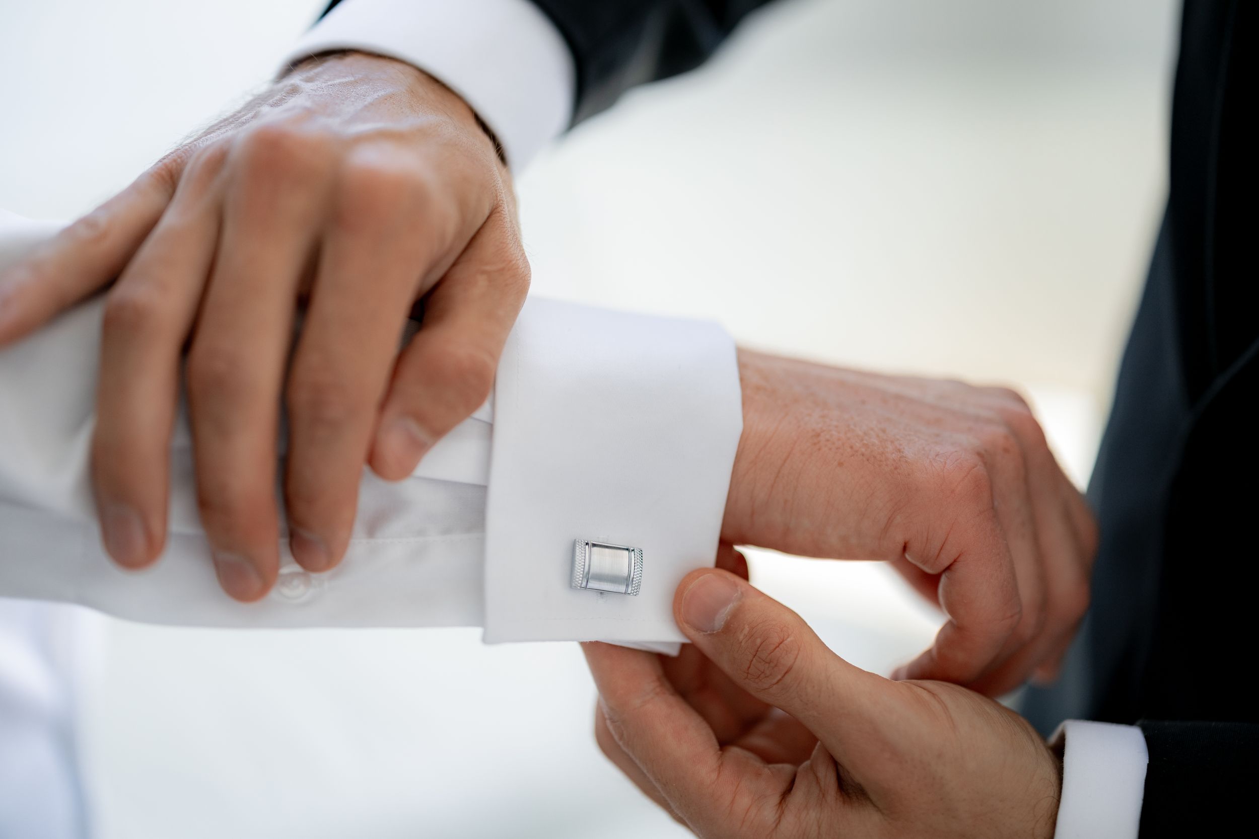 Close-up of hands adjusting silver cufflinks on white dress shirt.