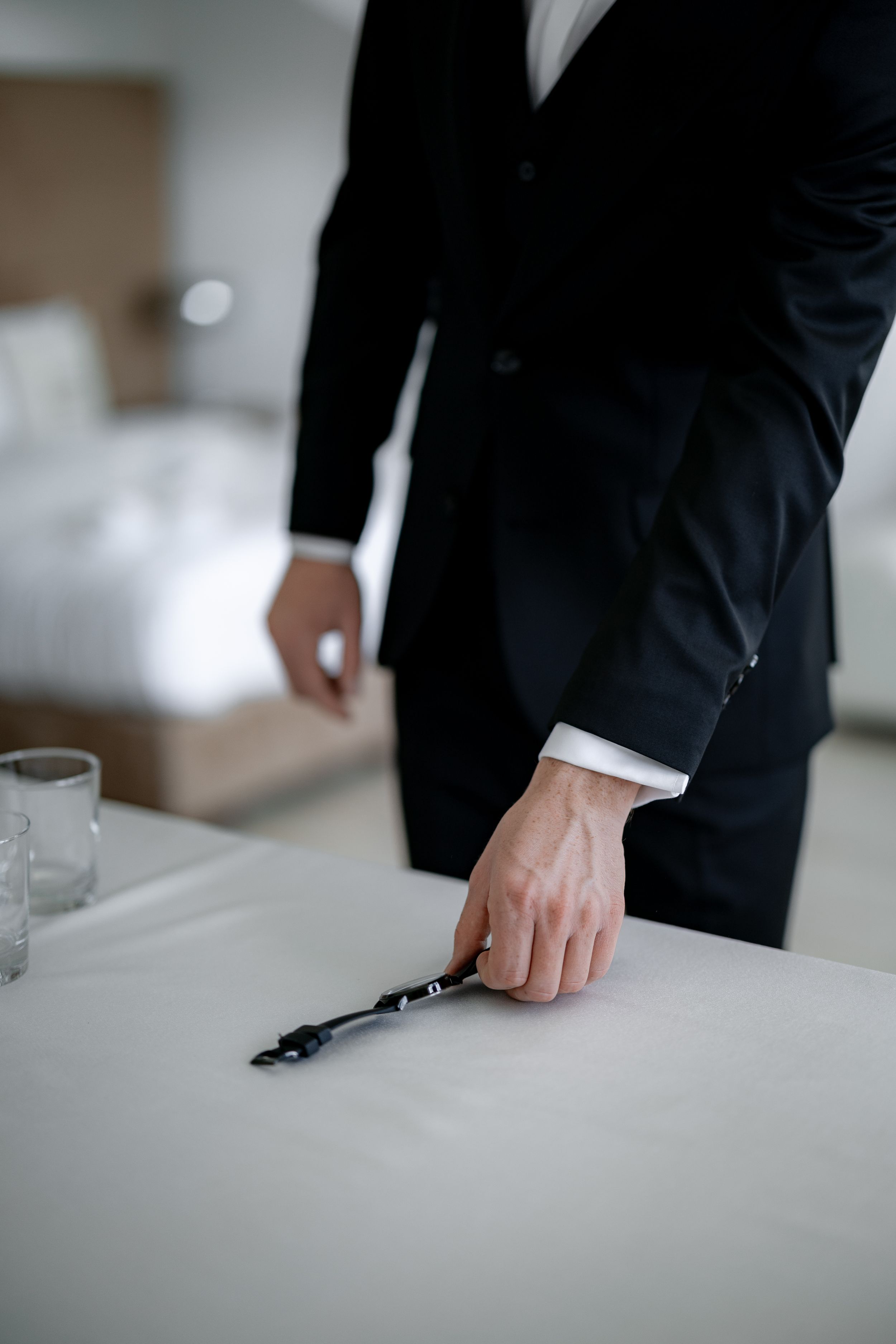 Man in tuxedo reaching for key on white table during wedding preparation.