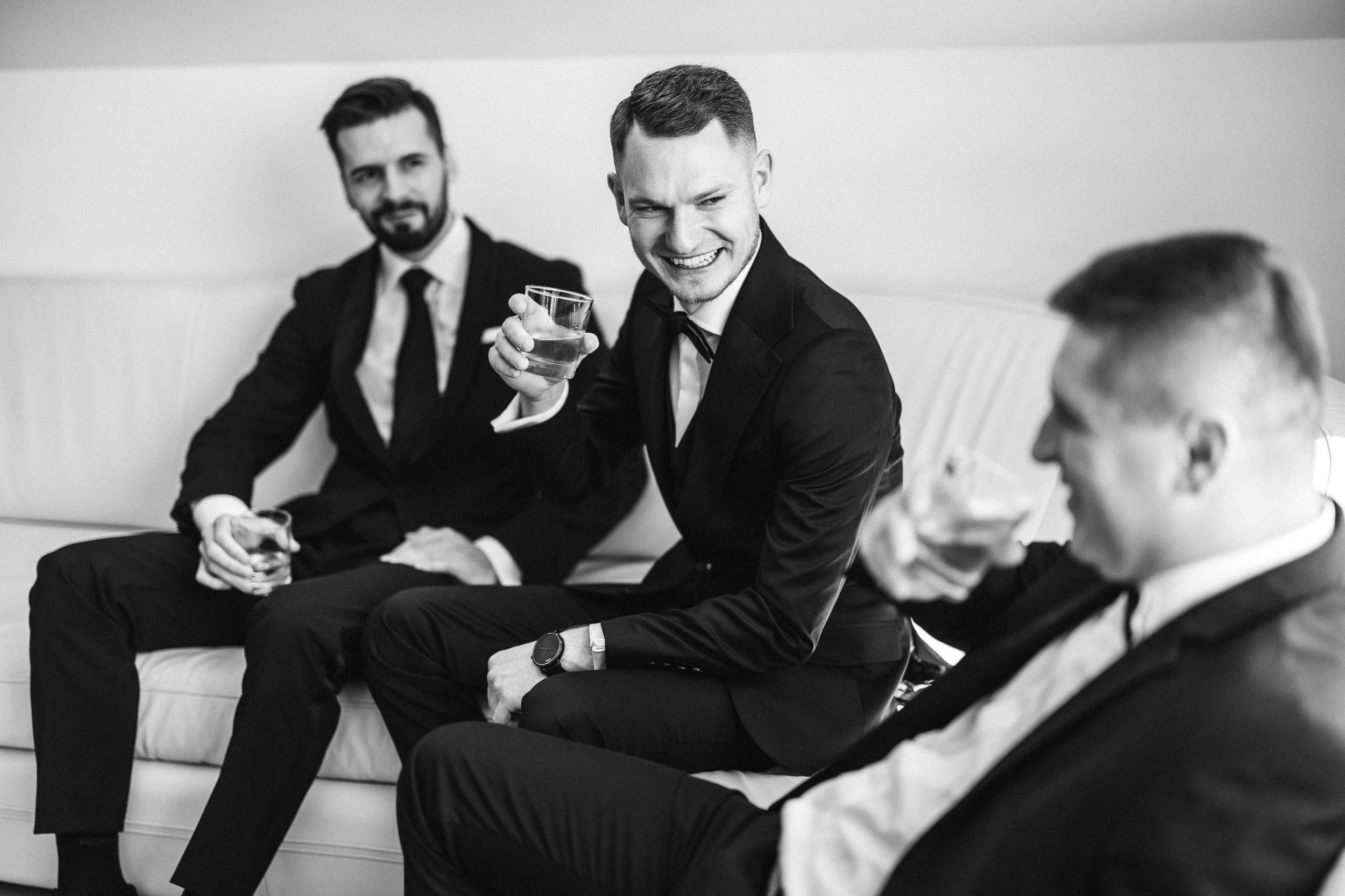 Groomsmen laughing and enjoying drinks together in black and white photography.