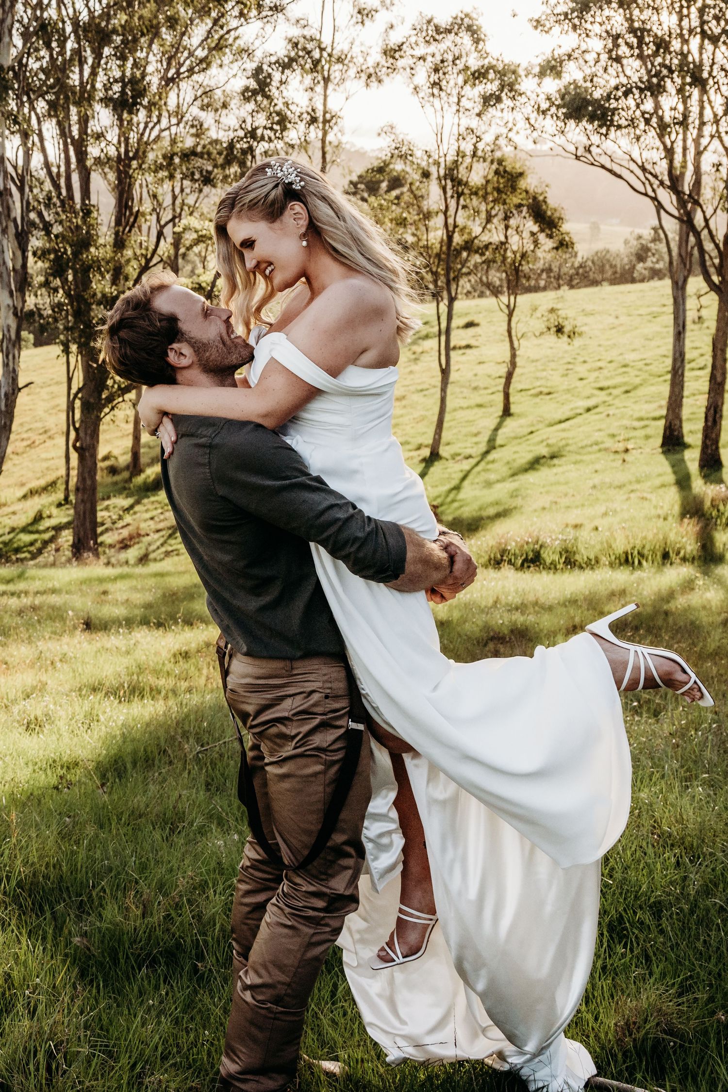Couple embracing in a scenic field with eucalyptus trees during a wedding photoshoot.