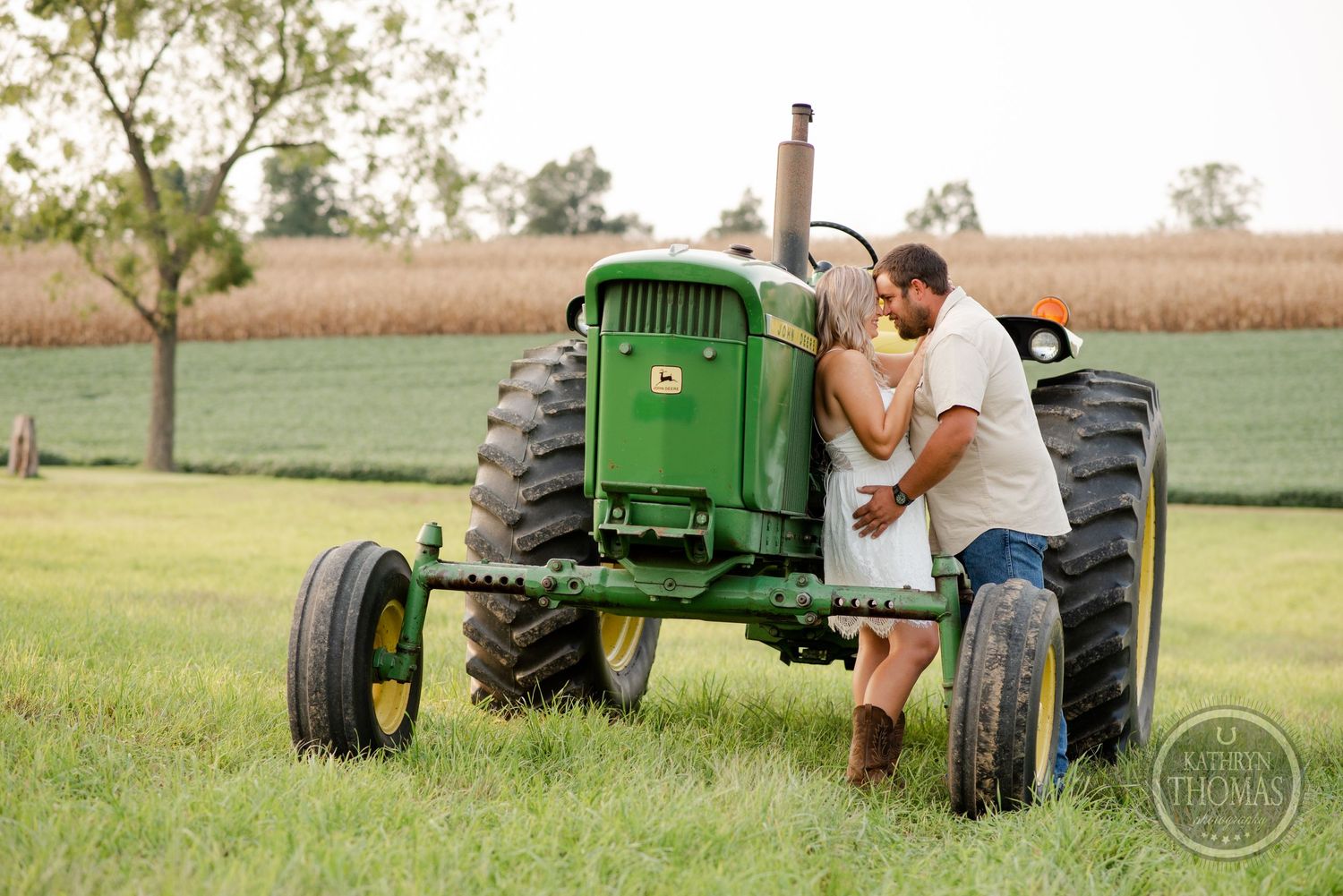 Couple shares romantic moment on classic green John Deere tractor in countryside setting.