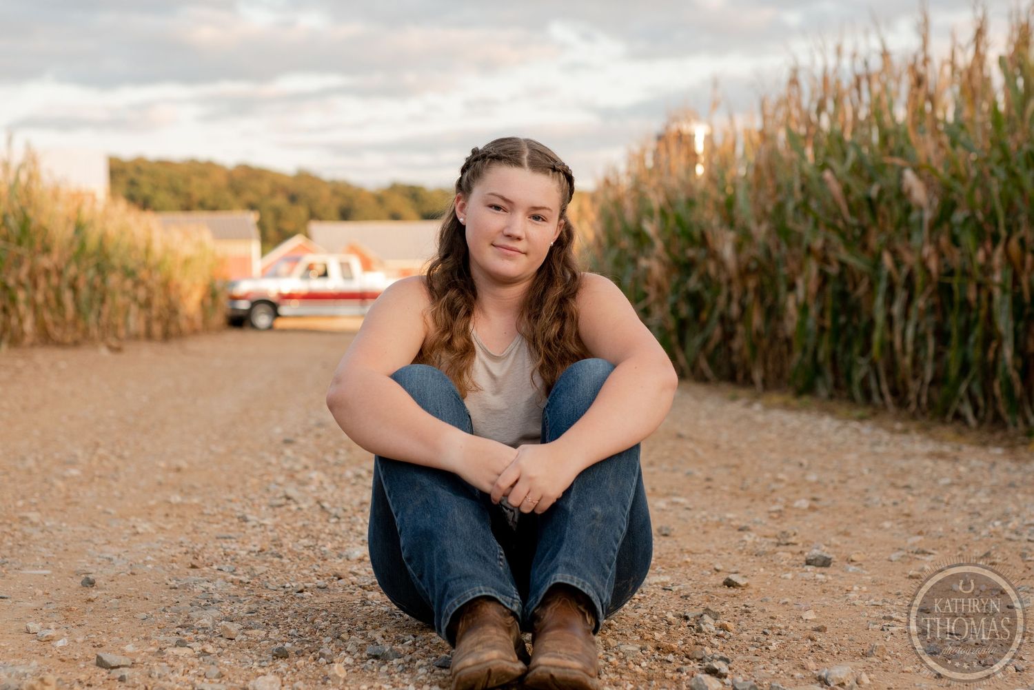 Sitting casually on a dirt path between tall cornfields at sunset.