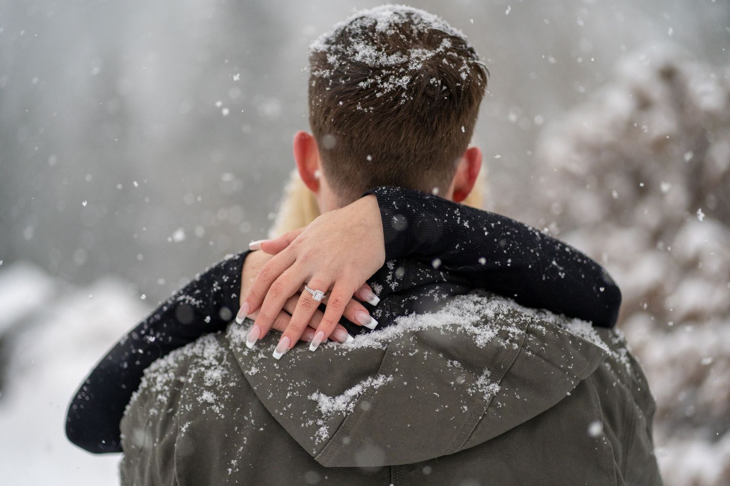 Close-up shot showing a ring on hand resting on shoulder during snowy weather.