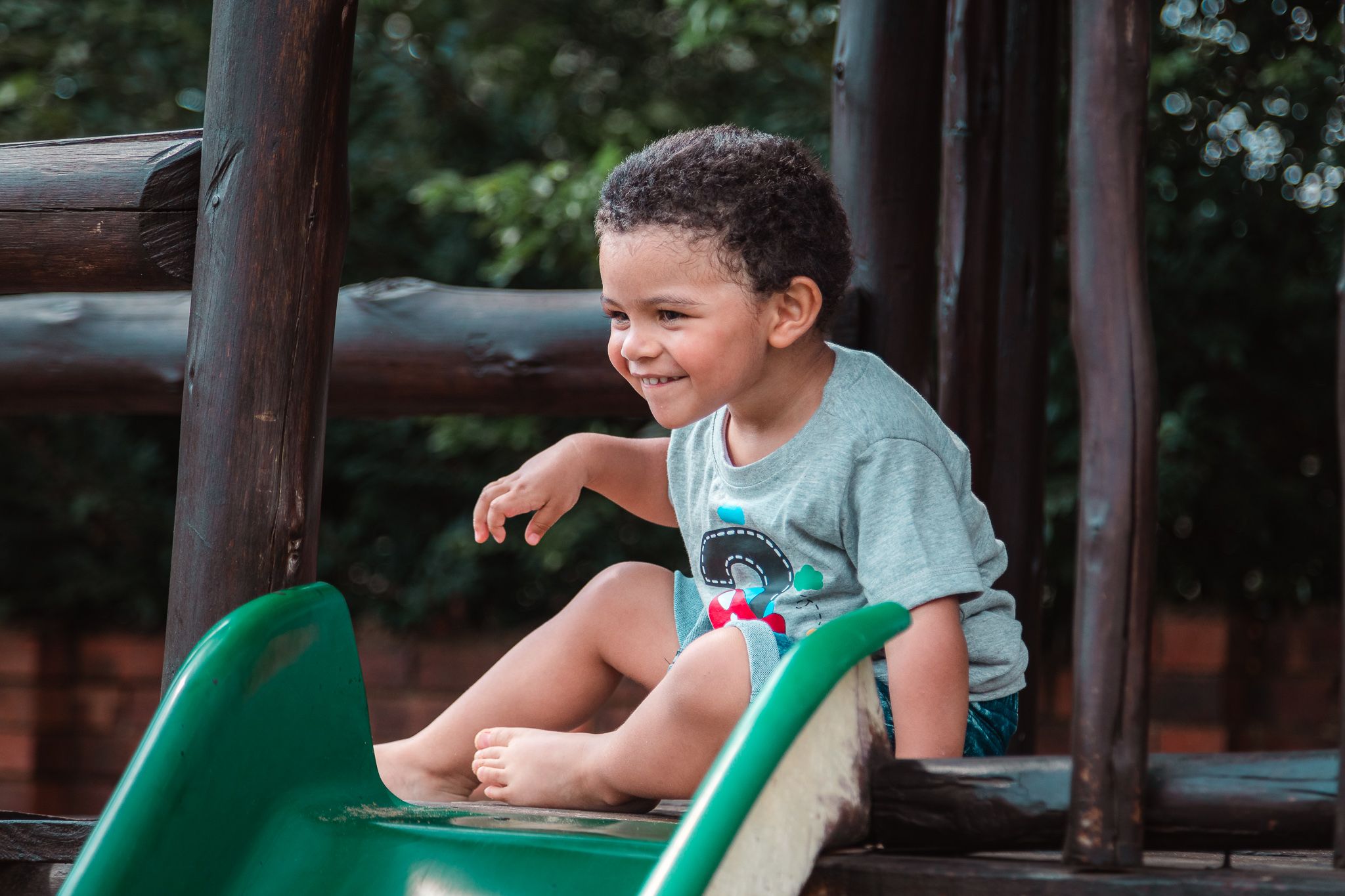 Cute young laughing boy at the top of a green slide getting ready to go down.