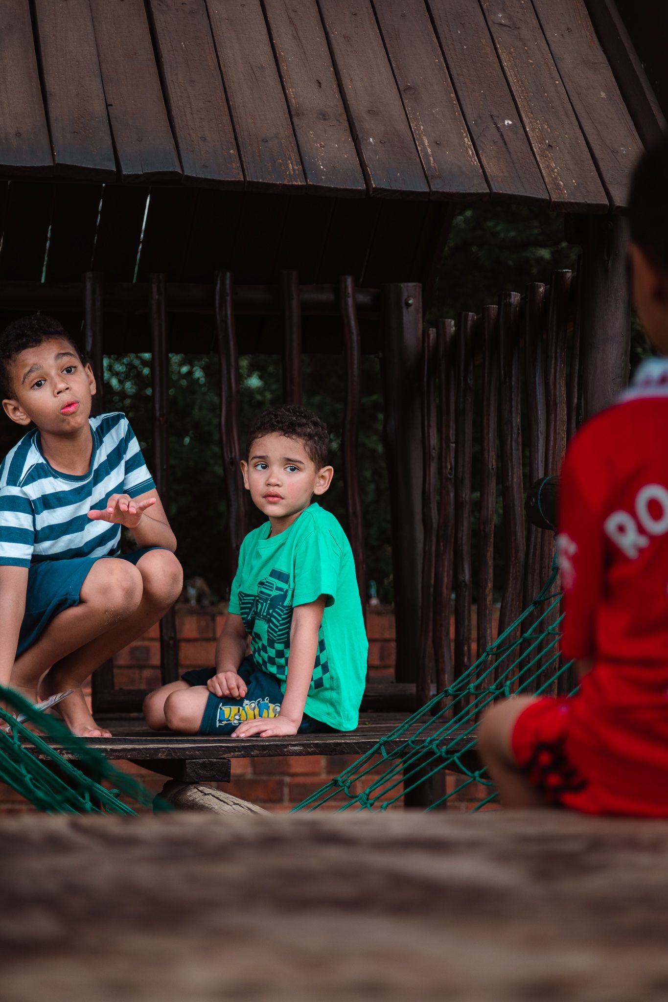 Three young boys in colourful clothing engaging in conversation on a wooden climbing frame