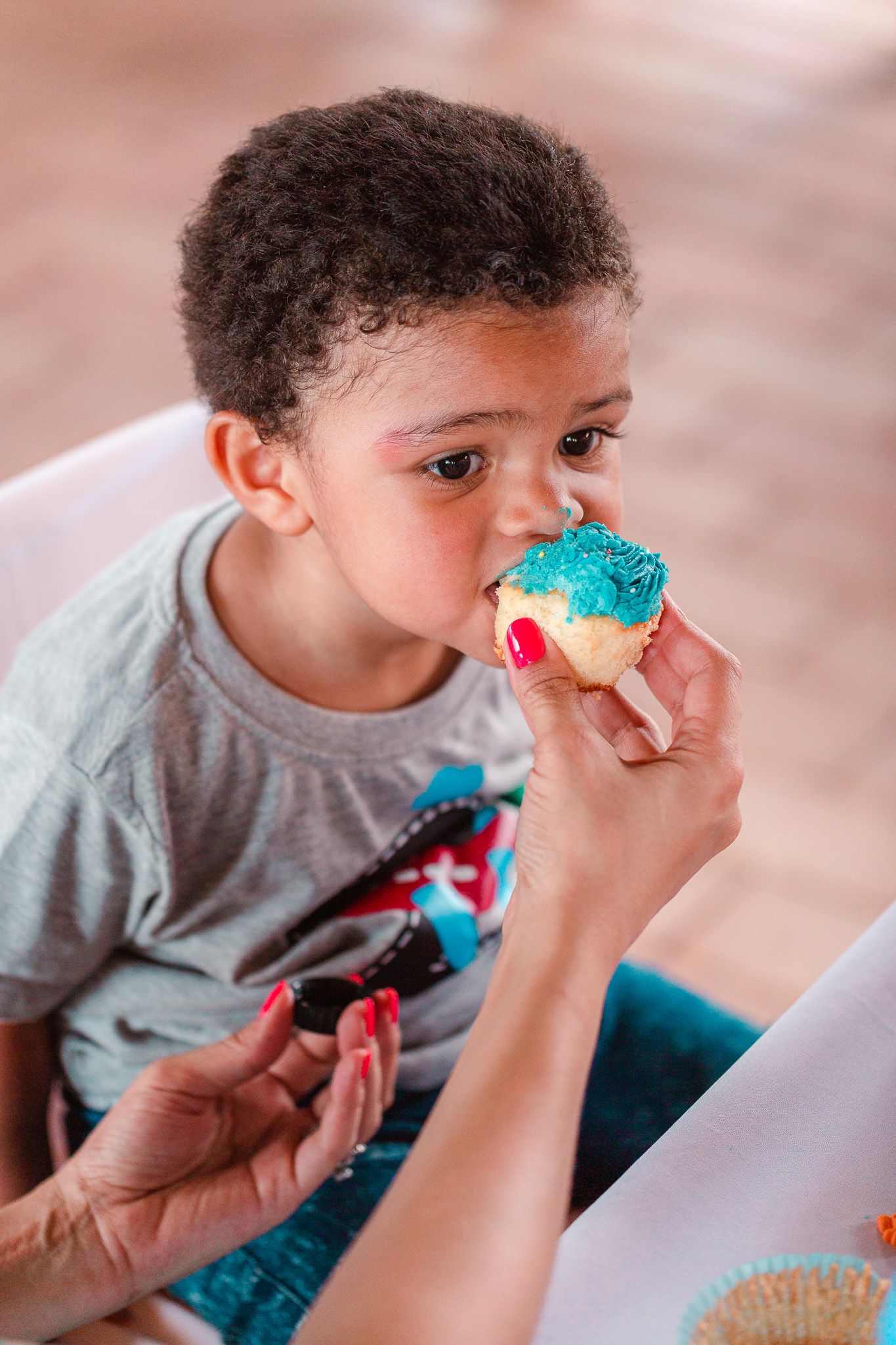 Mom's hand reaching out to give her young son a bite of his blue birthday cupcake.