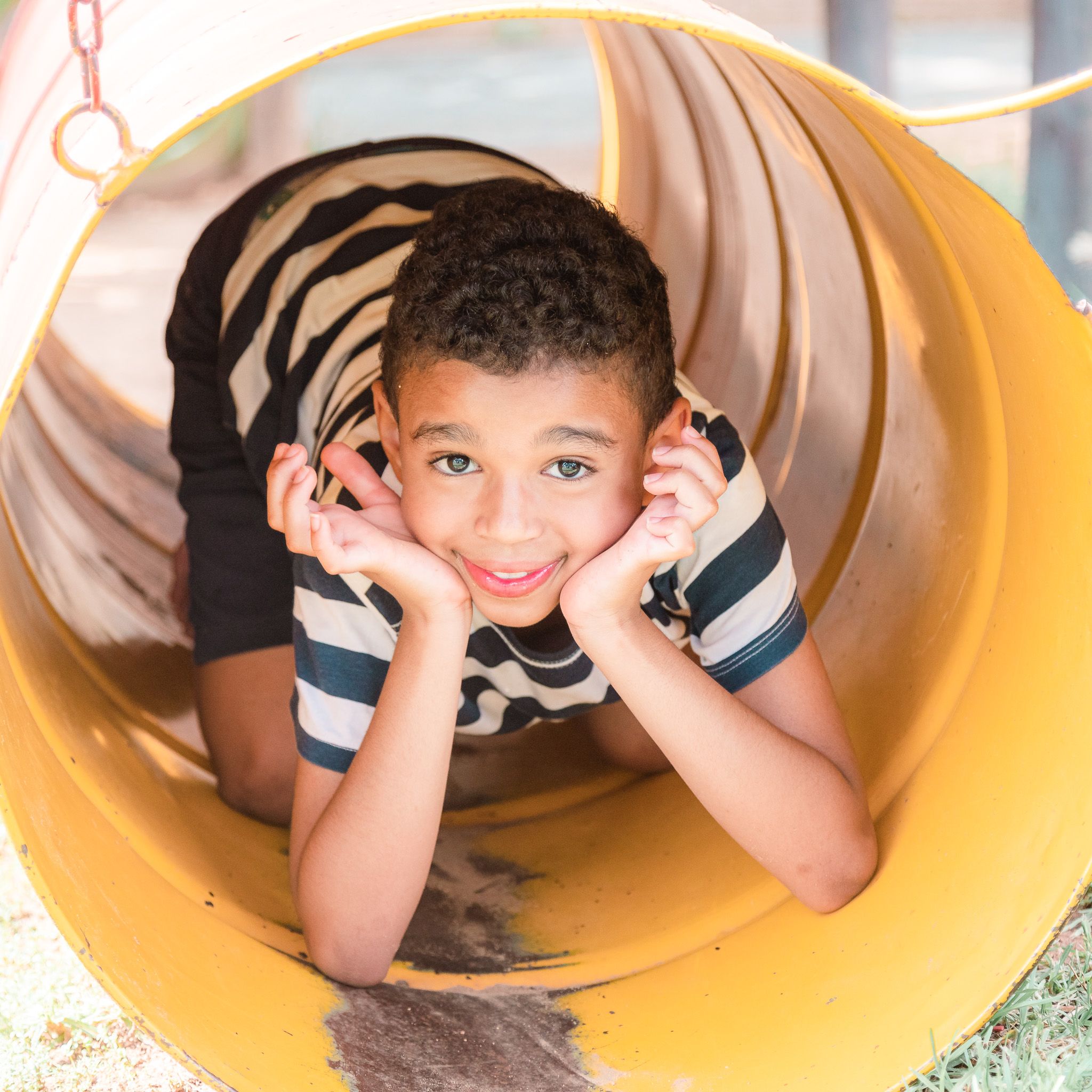 Cute young smiling boy in striped t-shirt inside a yellow barrel at a playground