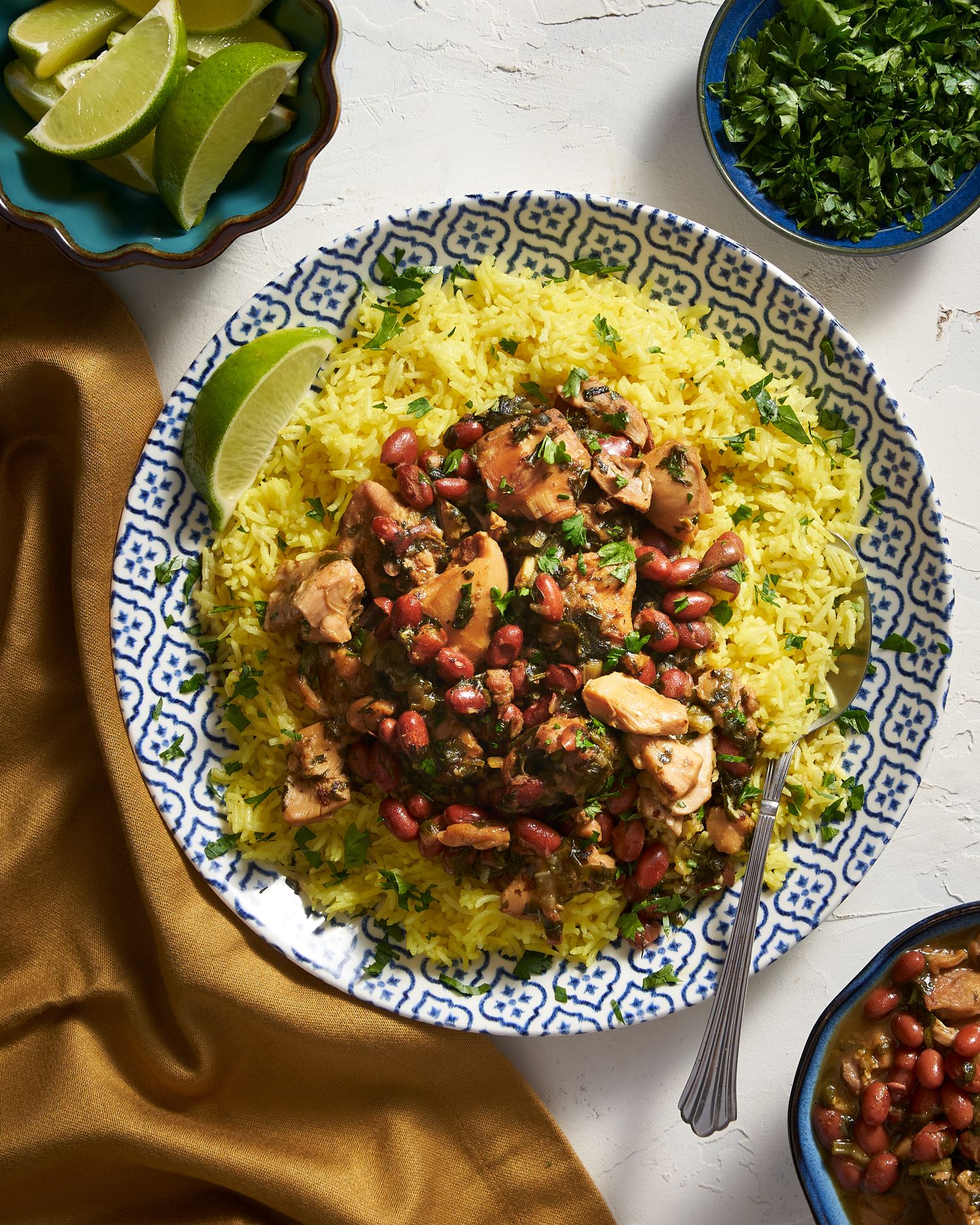 Yellow saffron rice topped with braised chicken and garnished with fresh herbs and lime wedges served in a patterned bowl.