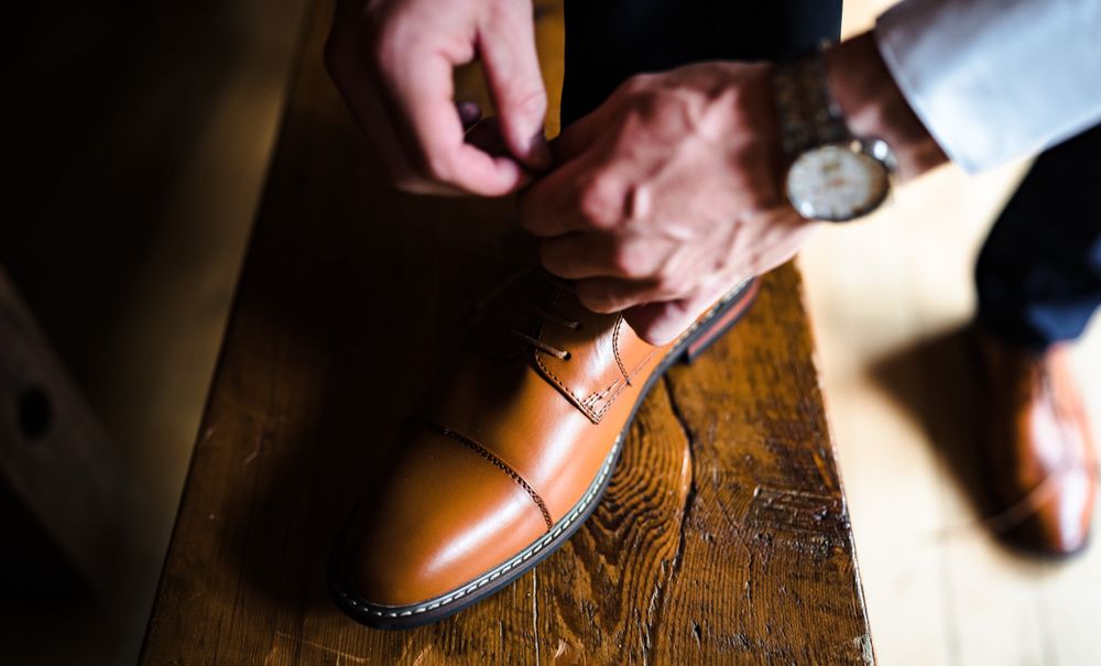 Brown leather dress shoes being polished on wooden floor.