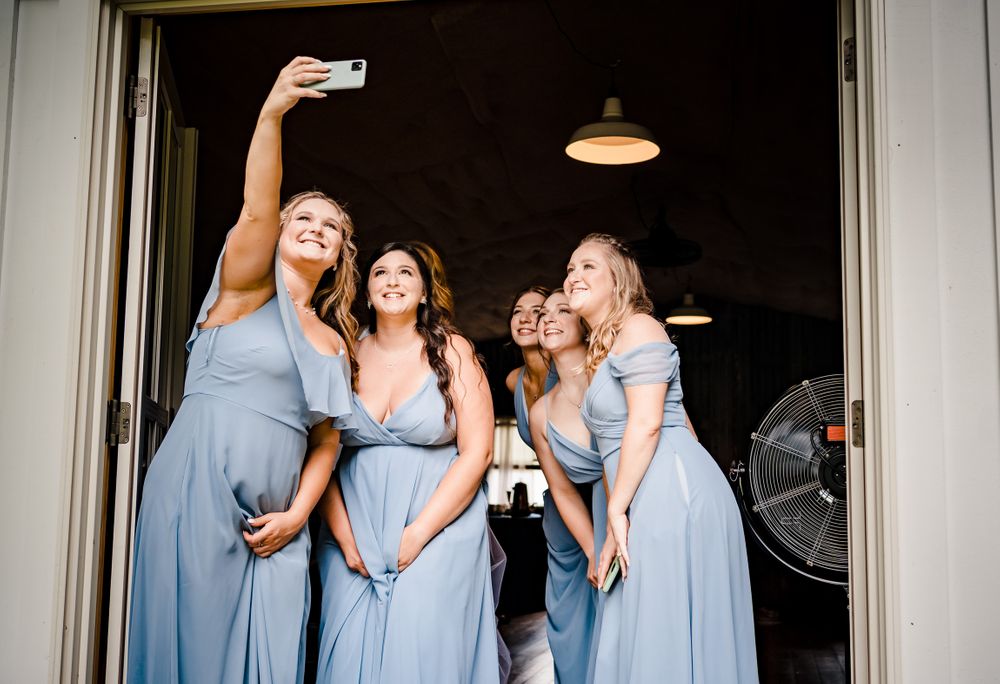 Bridesmaids in light blue dresses taking selfies and sharing laughs during wedding preparations.