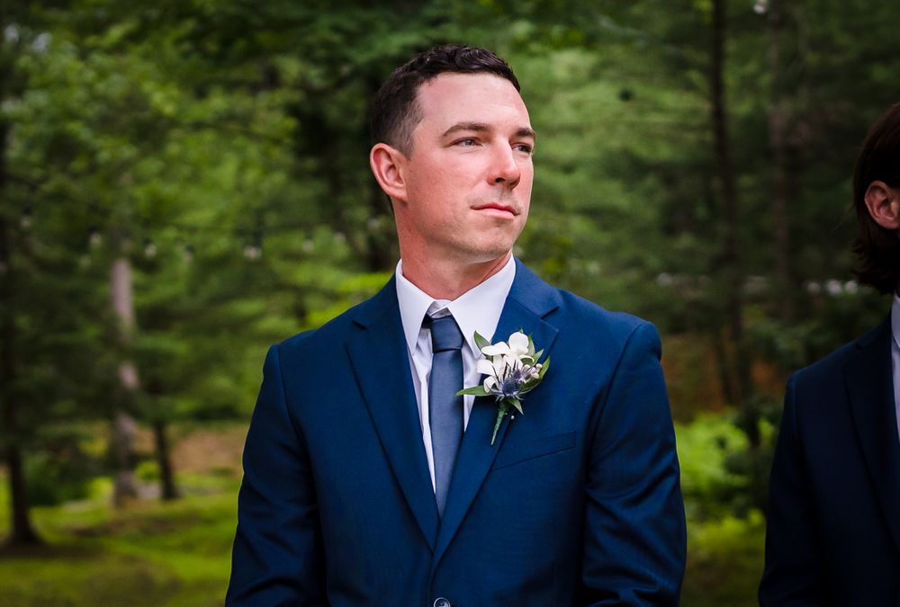 Groomsmen in navy suits lined up outdoors during a summer wedding.