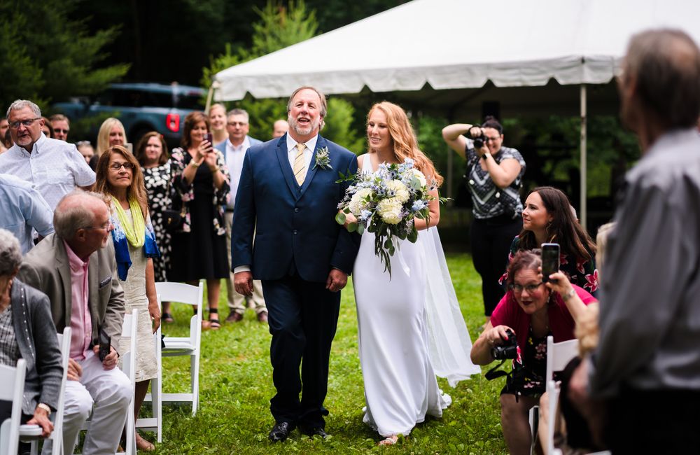 Wedding celebration with guests gathered on a green lawn under a white tent.