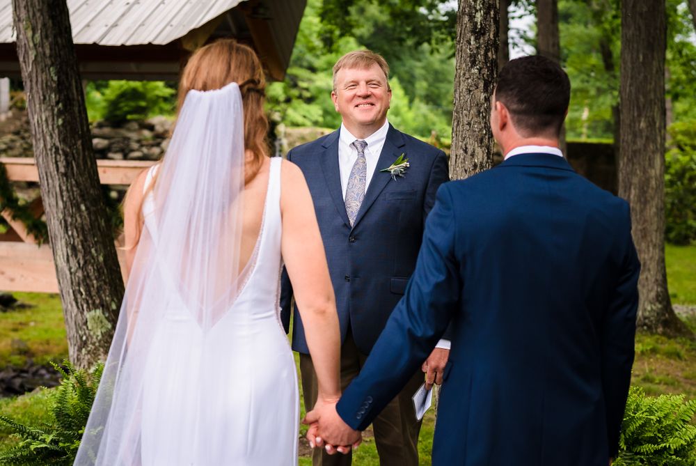 Outdoor wedding ceremony taking place among tall pine trees and natural landscaping.
