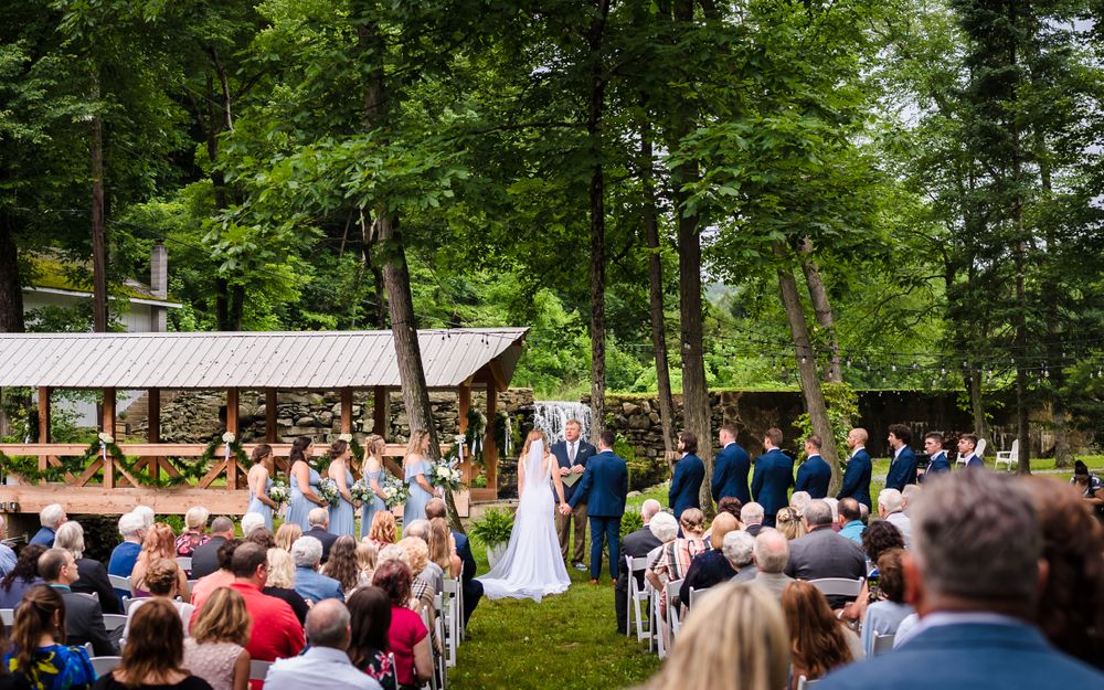 Panoramic view of outdoor wedding ceremony with guests seated among tall trees.