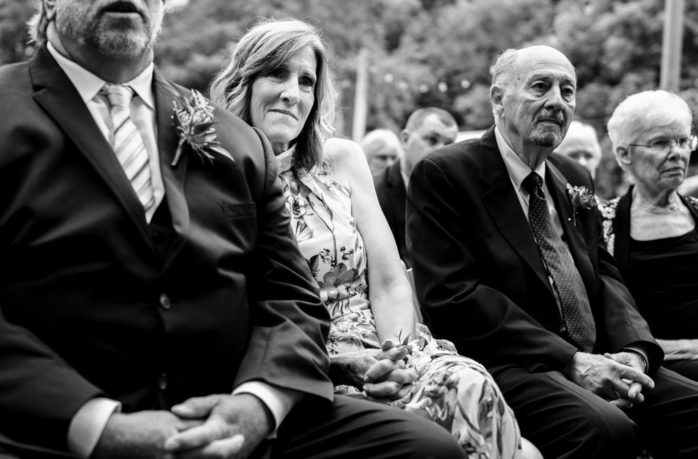 Wedding guests seated in rows watch the outdoor ceremony with joyful expressions.