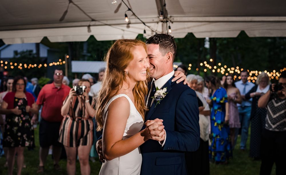 Evening wedding reception with couples dancing under tent and string lights.