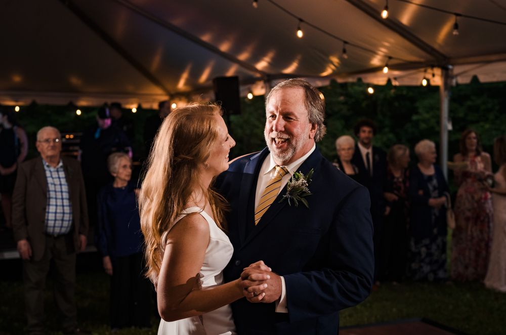 Wedding guests enjoying dance floor under tent with string lights at night.