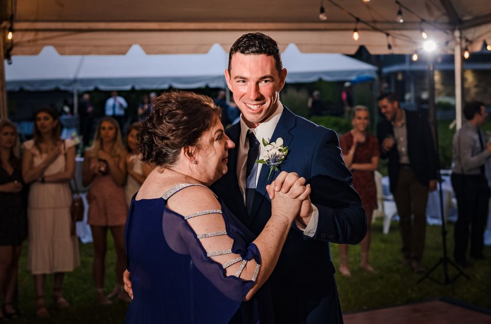 Couples dancing at evening wedding reception under tent with ambient lighting.