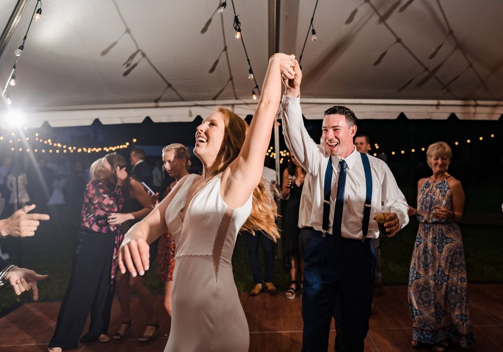 Wedding reception dance party under tent with dramatic lighting and festive atmosphere.