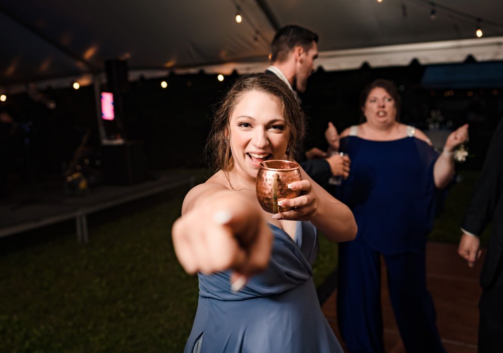 Guest raises a drink in celebration at an outdoor wedding reception under string lights.