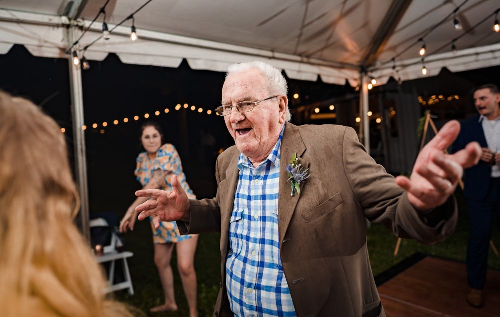 Senior guest dances enthusiastically at outdoor reception with string lights.