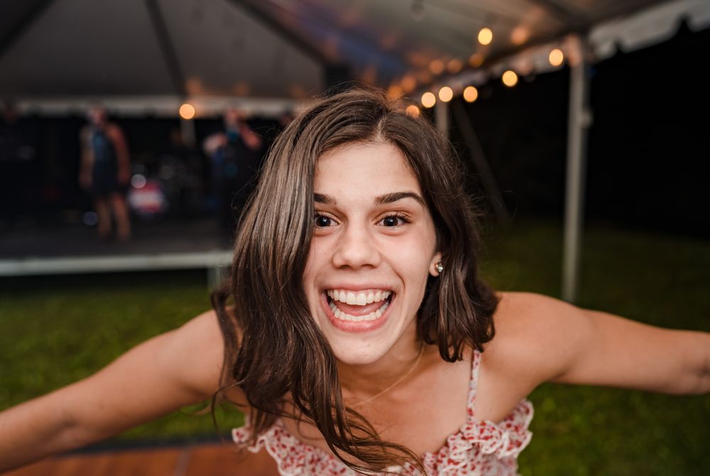Joyful party guest poses with arms spread wide under tent lighting.