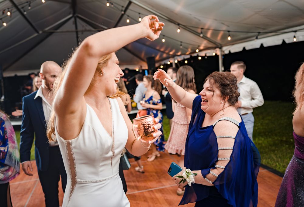 Wedding guests dancing and celebrating on wooden dance floor under tent.