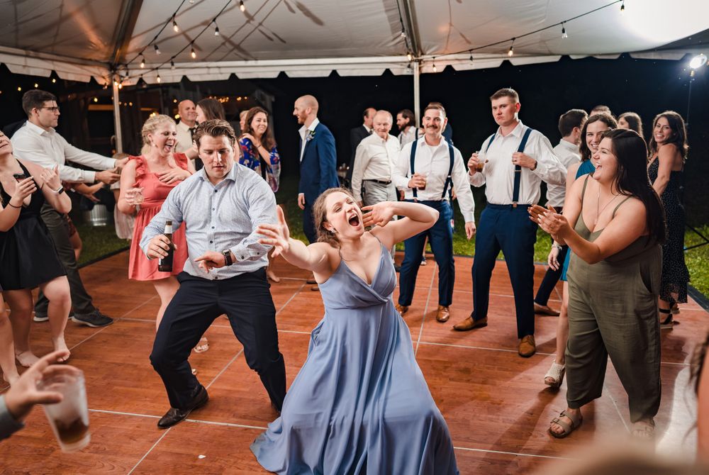 Group of wedding guests dancing energetically on wooden floor at reception.