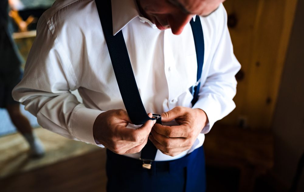 Close-up of formal attire showing white shirt, navy suspenders and tie details.