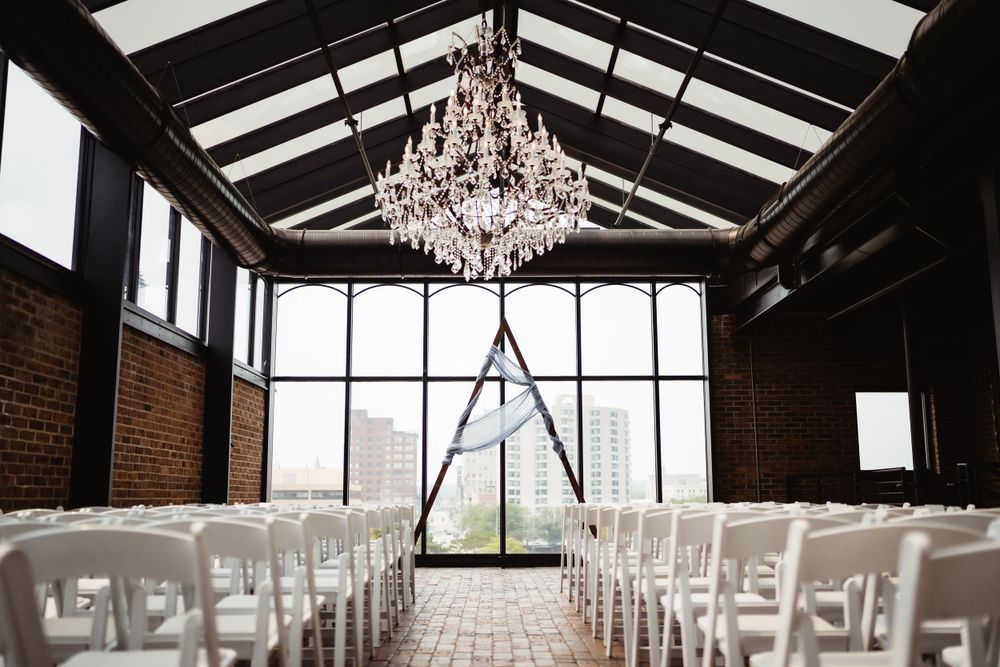 Elegant wedding ceremony venue with crystal chandelier and white chairs in industrial space with exposed brick walls.