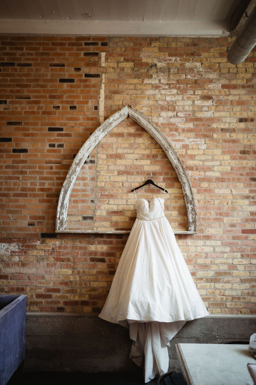 White wedding dress hanging on rustic brick wall with arched architectural detail.