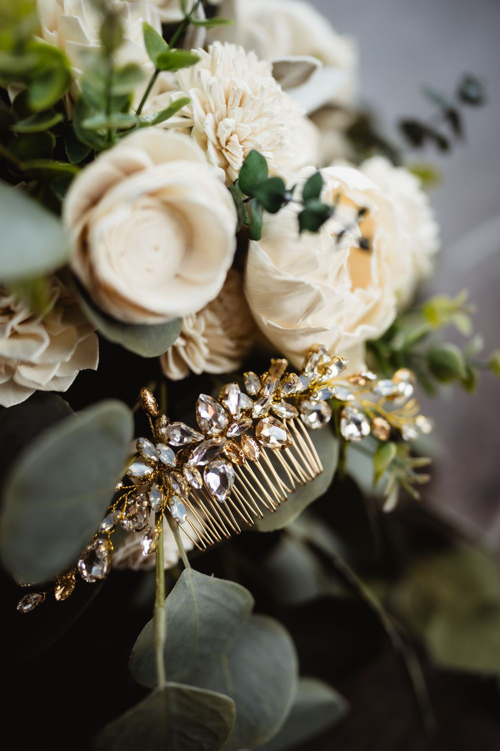 Elegant bridal hair accessory with crystal details nestled among cream roses and eucalyptus.