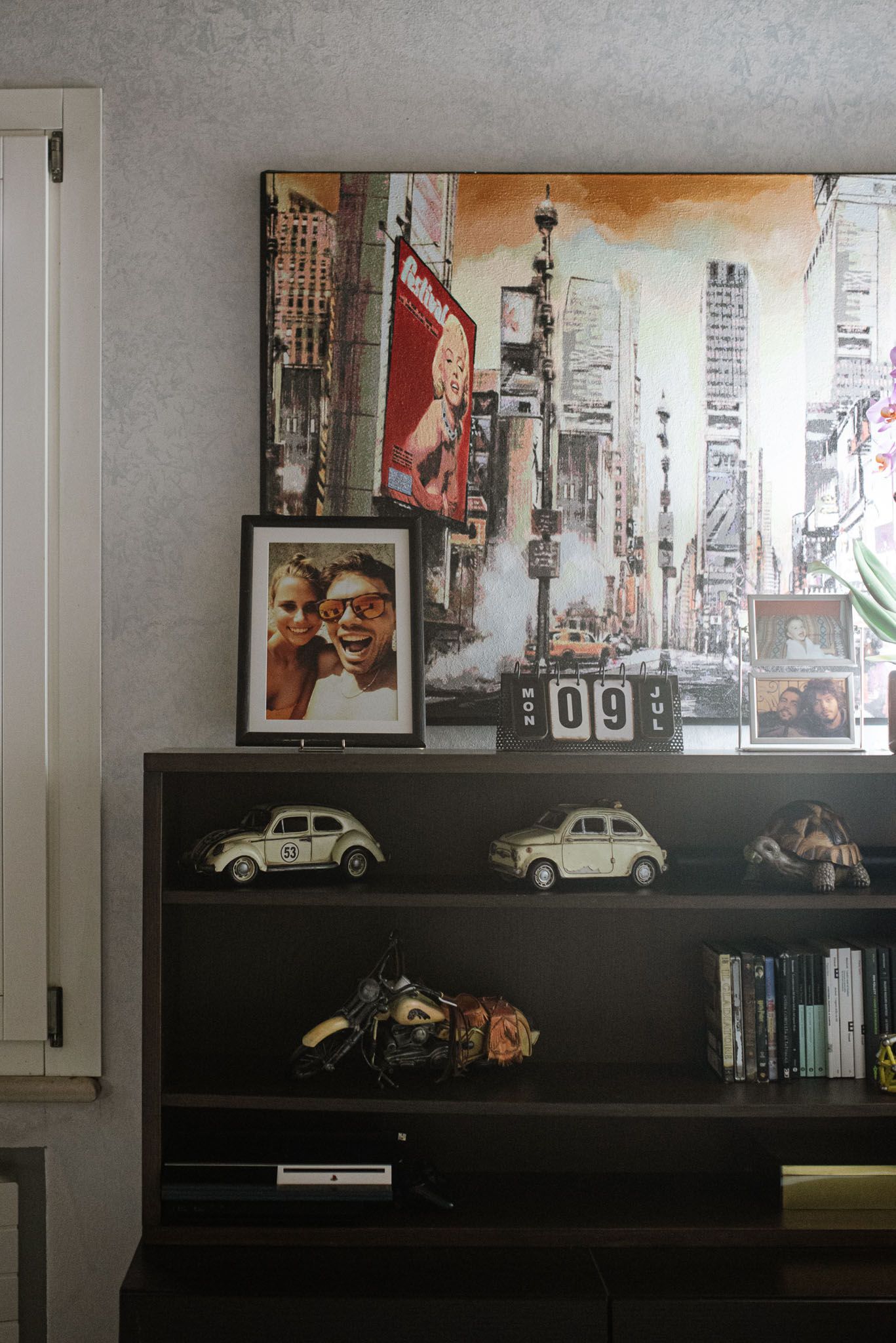 A modern shelf display featuring vintage toy cars, urban artwork, and personal photographs.