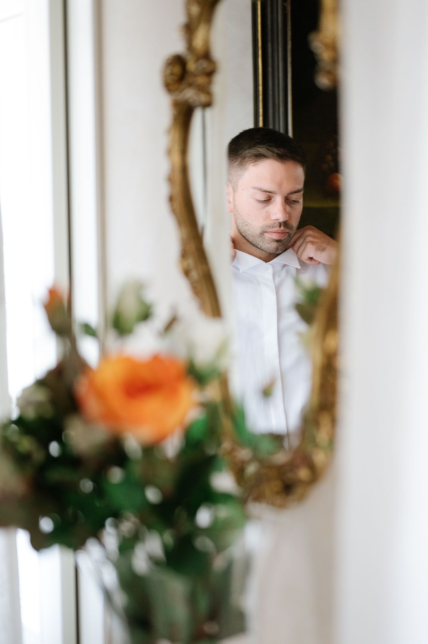 An artistic shot of a groom preparing for his wedding, reflected in an ornate gold mirror.