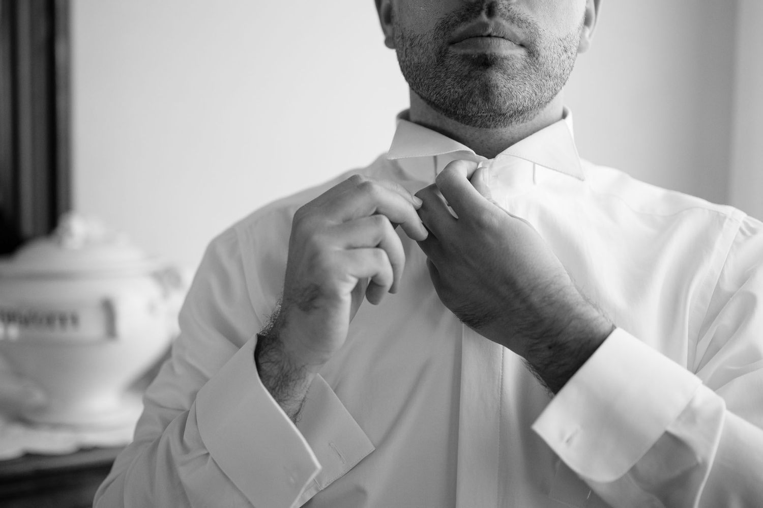Close-up shot of hands adjusting a white dress shirt collar and tie.