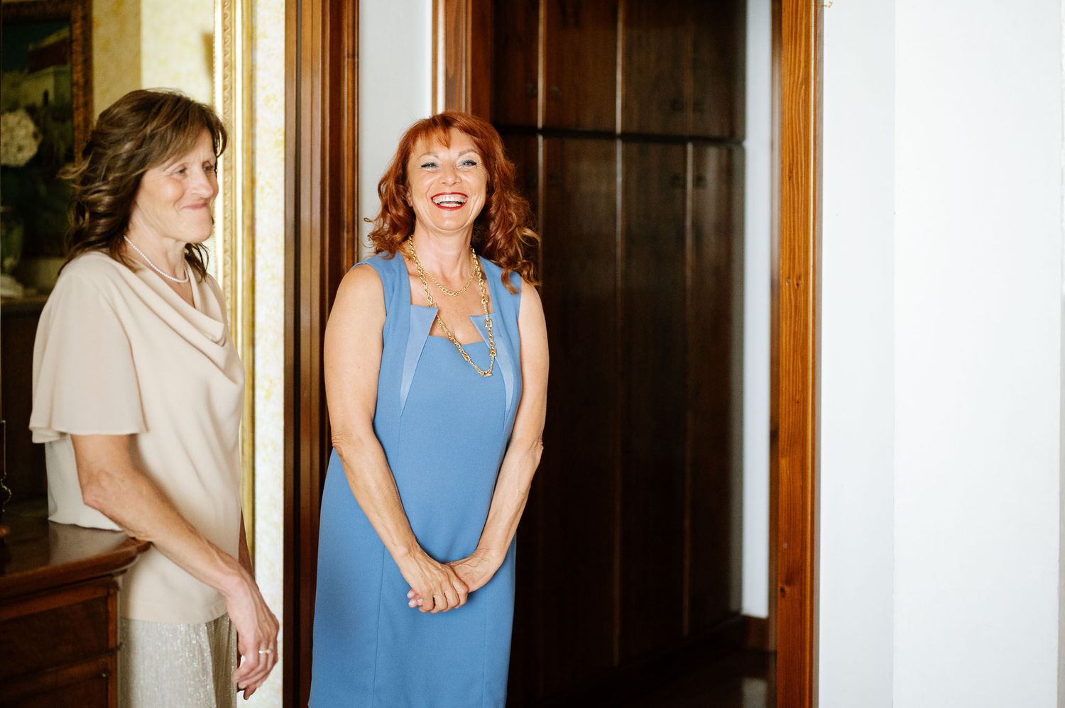 Two people share a joyful moment in hallway, one wearing blue dress.