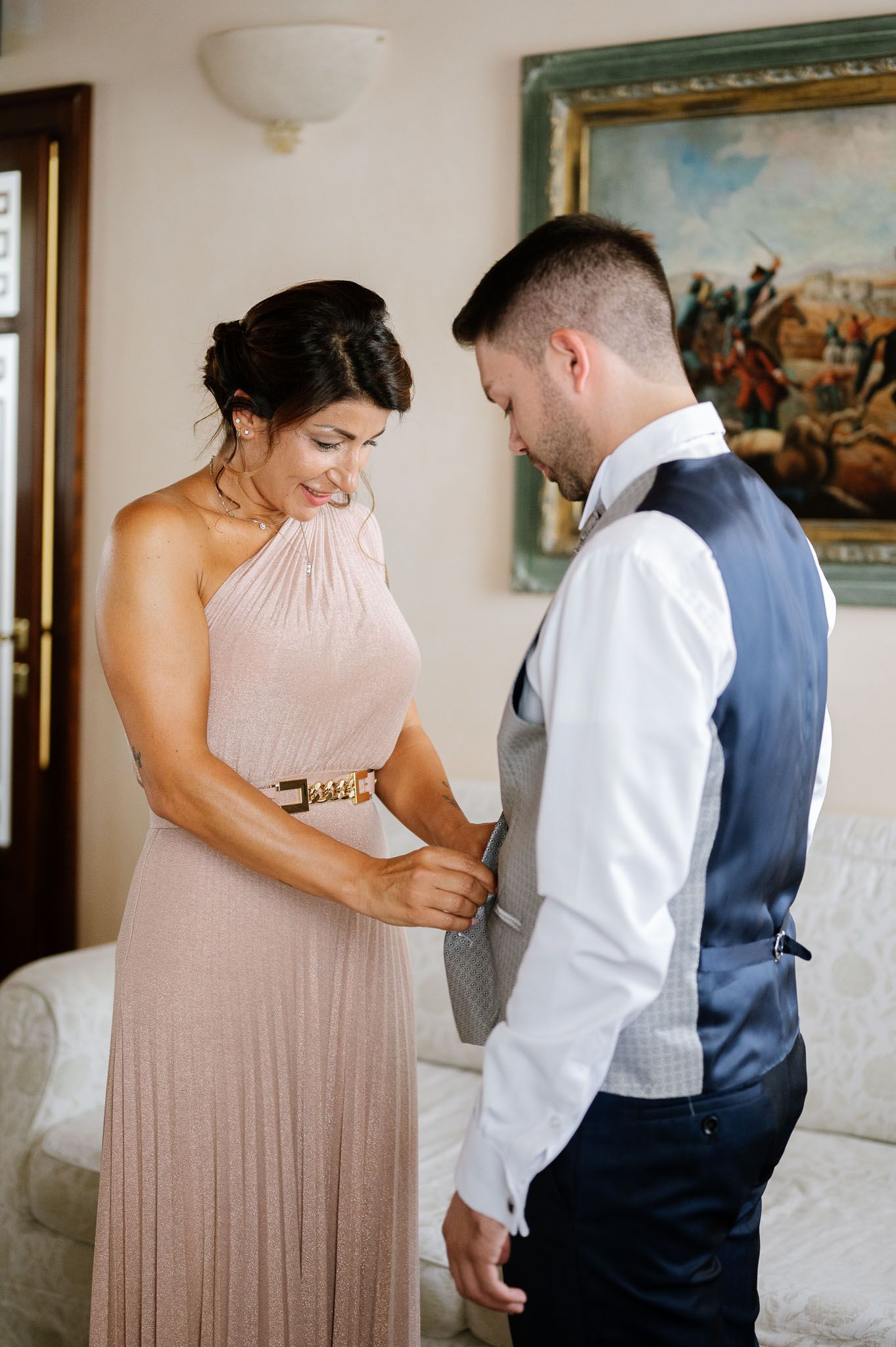 Wedding party members helping with formal attire preparations indoors.