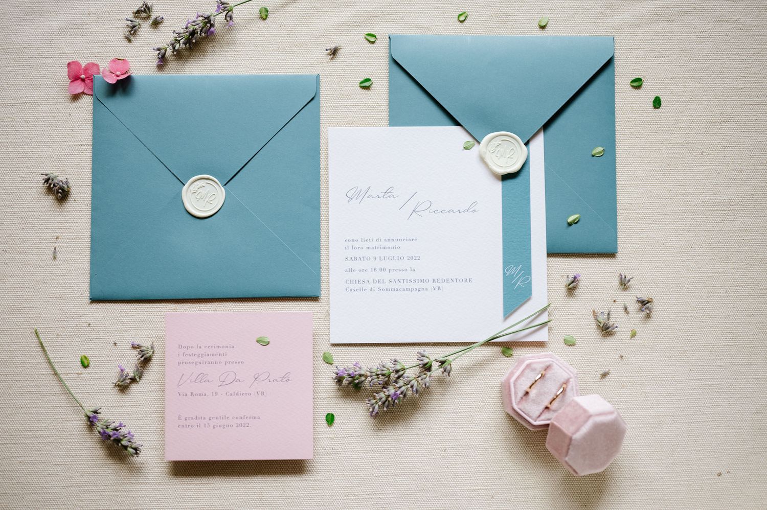 Elegant blue wedding invitations with wax seals arranged with dried flowers on a light surface.
