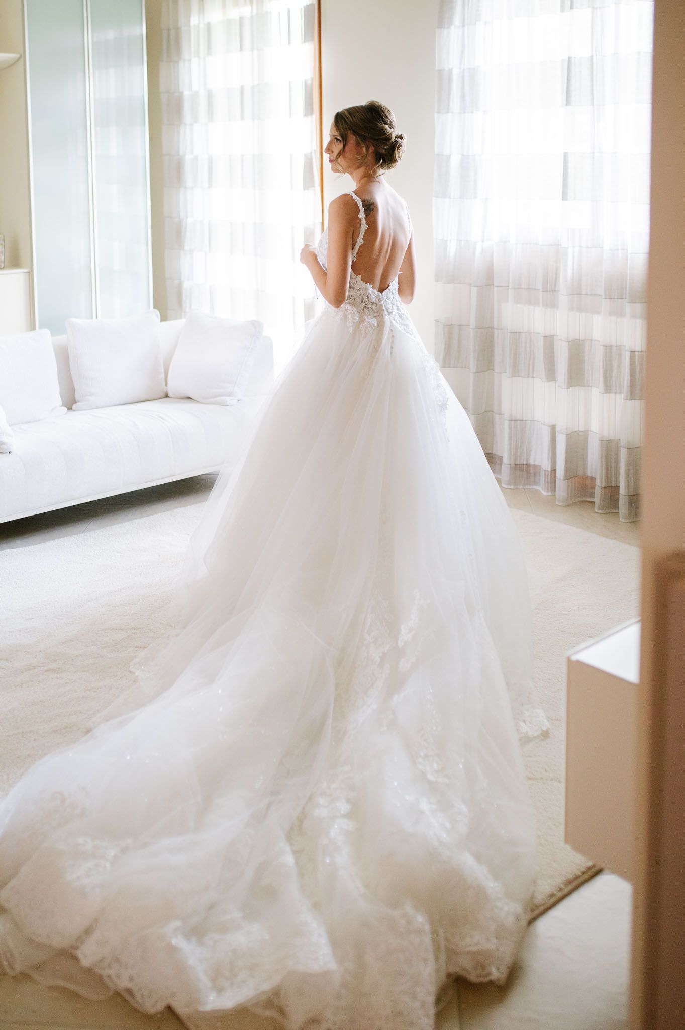 A flowing white wedding gown with lace details and open back photographed in a bright room.