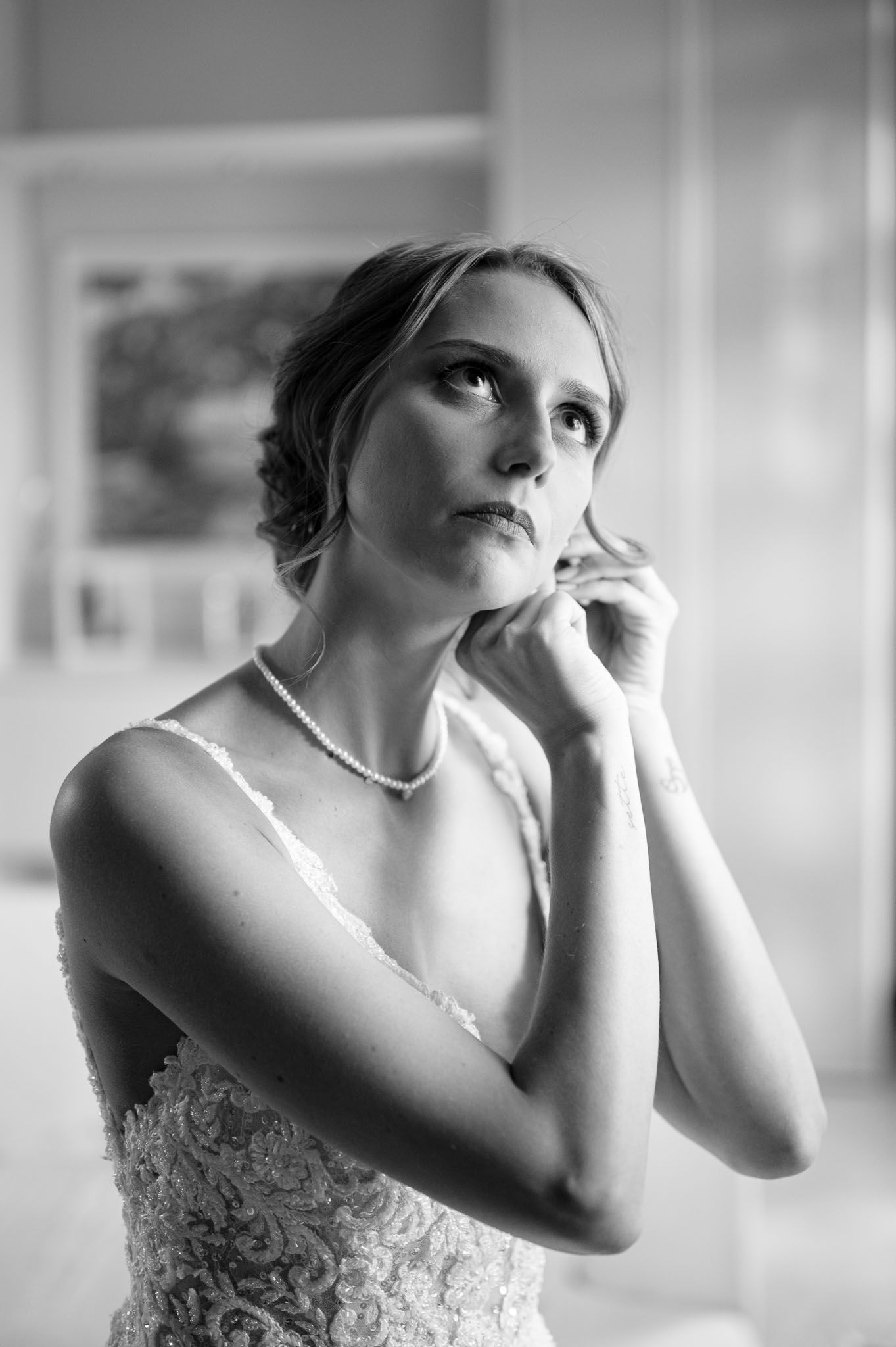A pensive moment captured in black and white of a bride wearing a delicate necklace and lace dress.