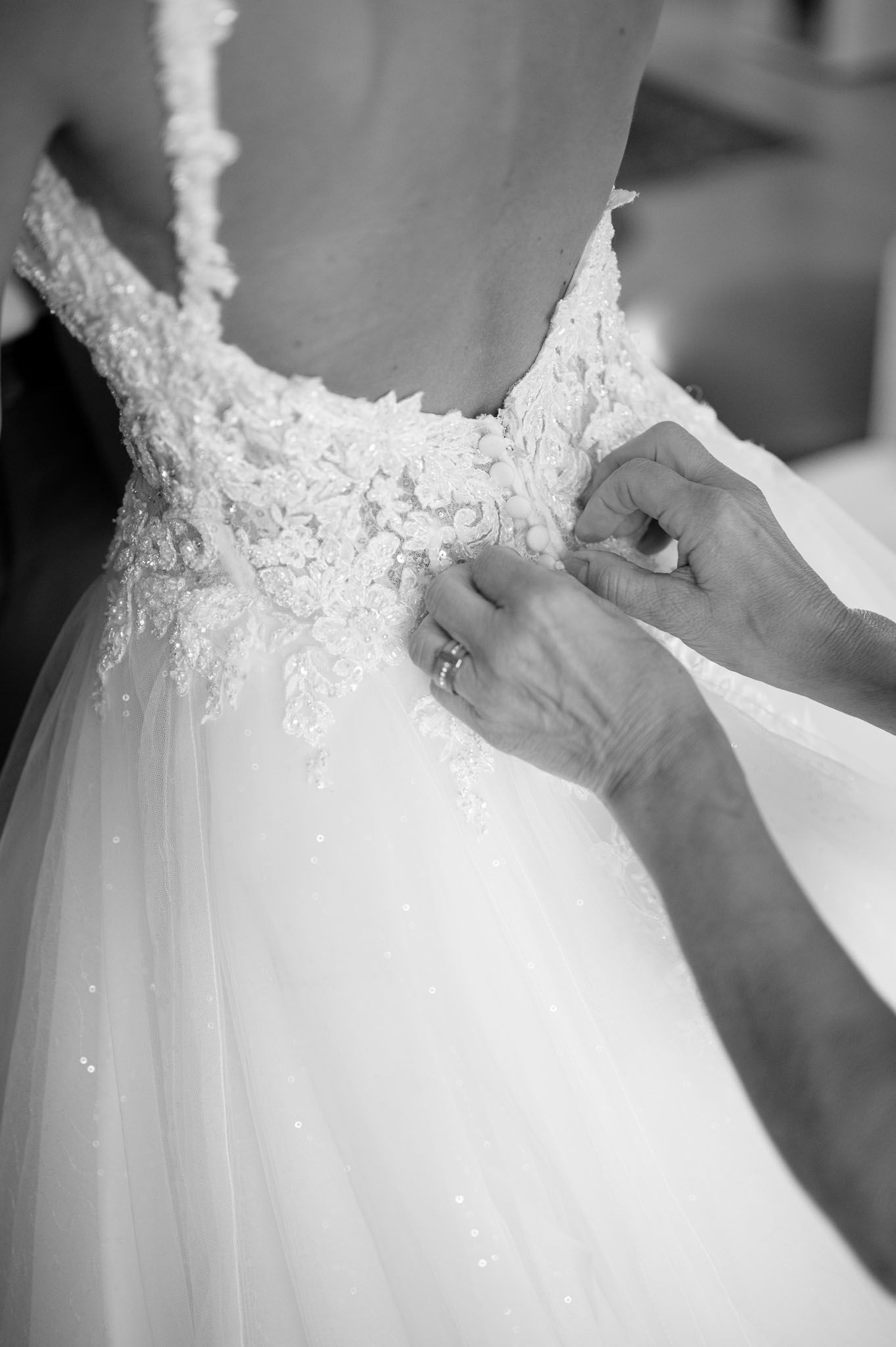 Close-up detail of hands fastening the back of a lace wedding dress.